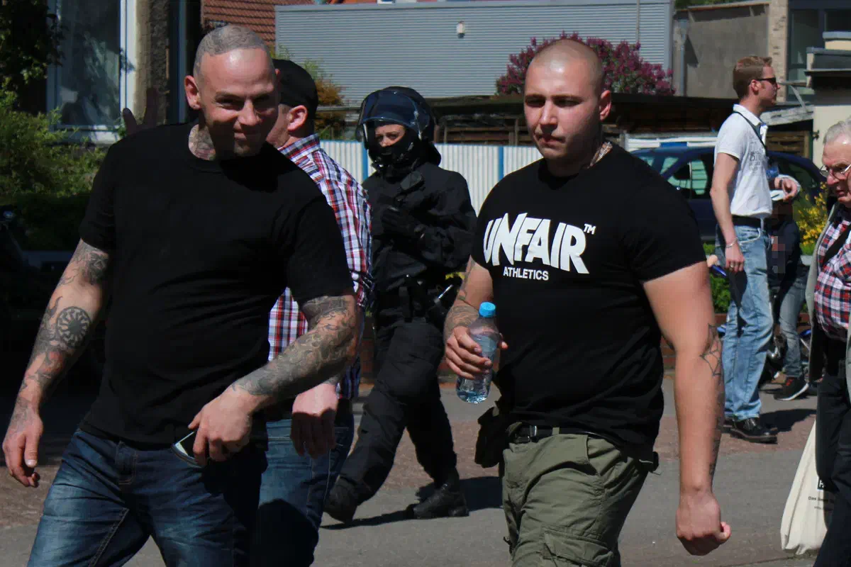 Der Teilnehmer links im Bild musste sein T-Shirt mit der neonazistischen Aufschrift „White Power“ auf links drehen. Das Symbol der „Schwarzen Sonne“ konnte er allerdings offen zur Schau stellen.