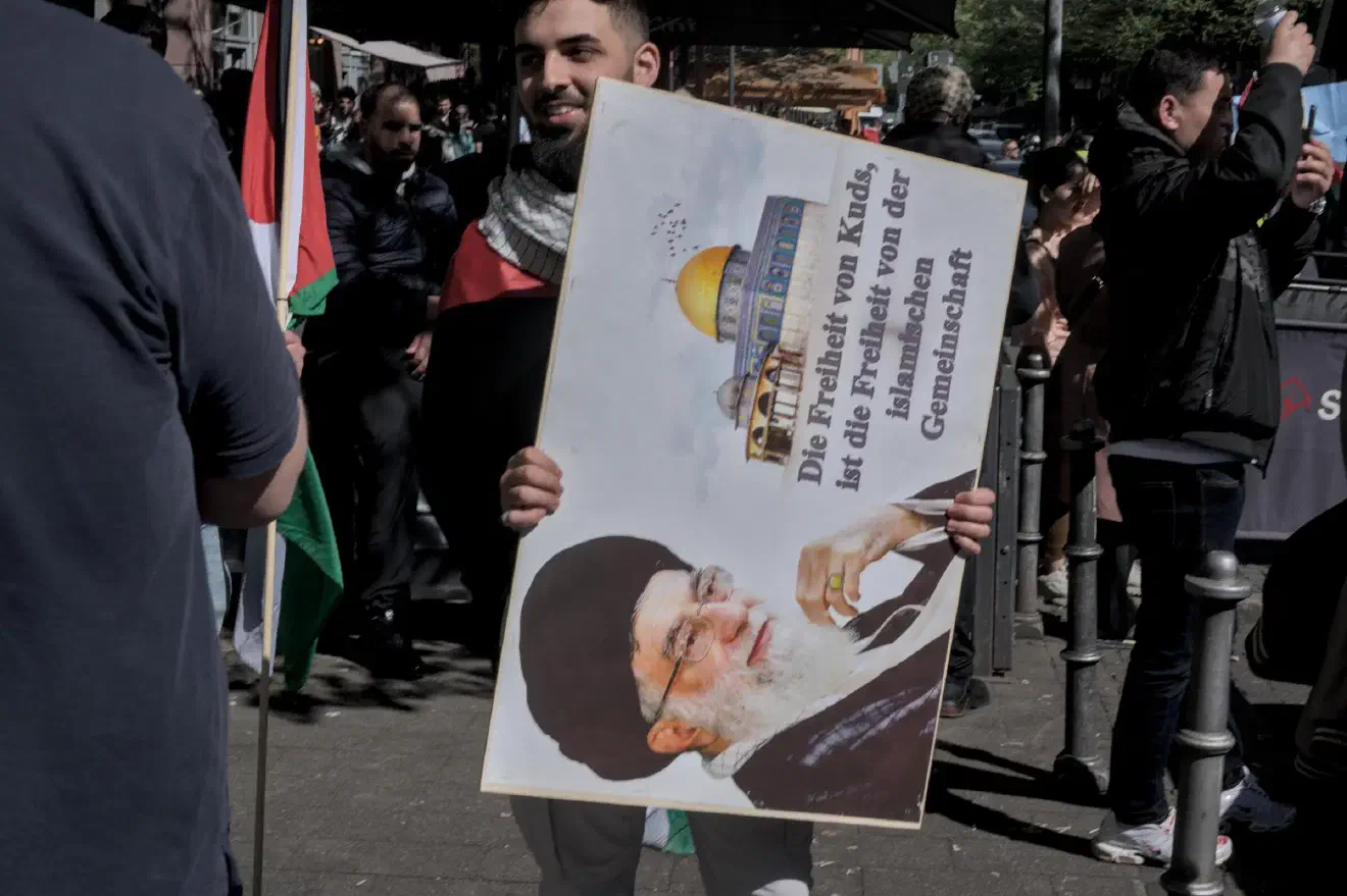Al-Quds ist das arabische Wort für Jerusalem. Die Person links auf dem Bild ist das aktuelle Staatsoberhaupt des Iran, Ajatollah Ali Chamenei.